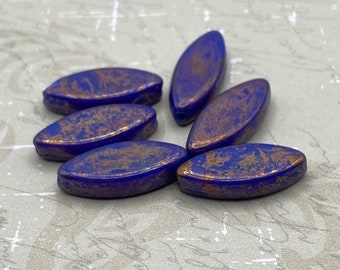 Six blue and gold Czech glass spindle beads arranged on a pale textured background.