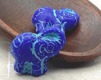 Two cobalt blue elephant beads with turquoise drip finish sitting on a dark wooden plate against a pale background.