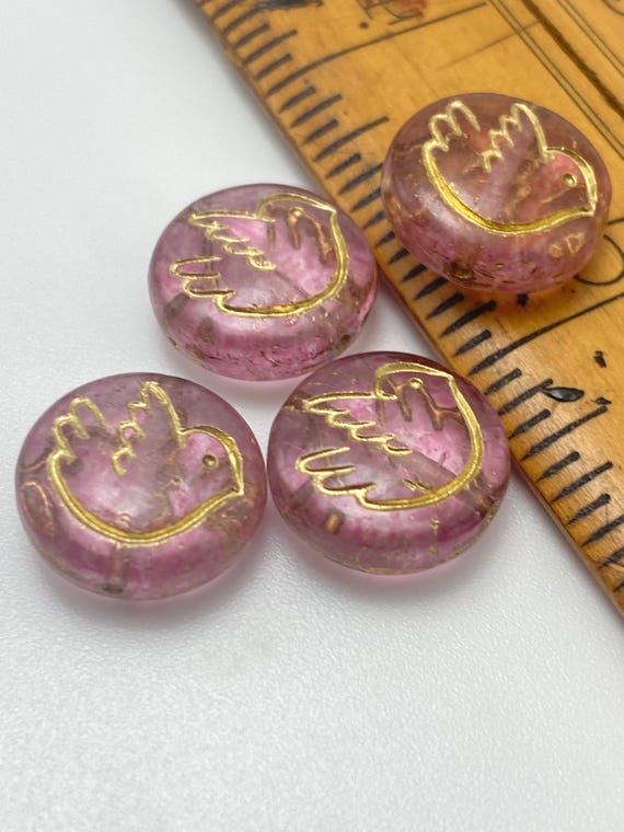 Four round Czech glass coin beads in clear pink with gold bird design, shown next to a ruler for scale.