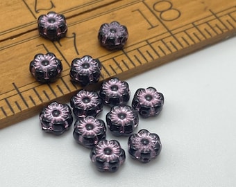 Twelve black and pink Czech glass flower beads displayed on a wooden ruler for scale.