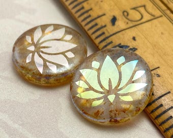 Two Czech coin beads with laser etched lotus flower design in cream and pale green, shown next to a wooden ruler for scale.