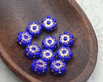 Twelve royal blue Czech glass flower beads with gold wash detail arranged on a dark wooden dish.