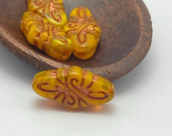 Four dandelion yellow Czech glass arabesque statement beads with copper wash detail, displayed in a wooden bowl.