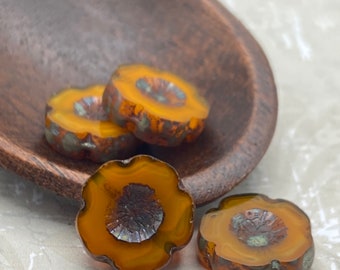 Four Czech glass Hawaiian flower beads in rustic orange picasso, displayed in a wooden bowl on a white linen background.
