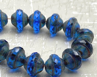 Eight sapphire blue Czech glass Saturn beads with Picasso finish arranged on a plain background, showing their faceted.