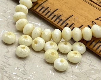 Czech glass rondelle beads in pale ivory with mercury finish arranged on a wooden ruler for scale.