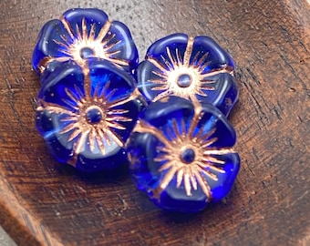Four royal blue Czech glass hibiscus flower beads with copper wash detail arranged on a wooden dish.