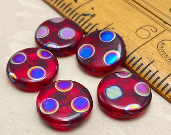 Five red Czech glass coin beads with iridescent peacock spot patterns, shown next to a wooden ruler for scale.