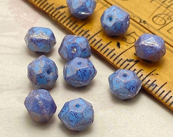 Nine blue Czech glass English cut beads with purple lustre finish arranged next to a yellow ruler for scale.