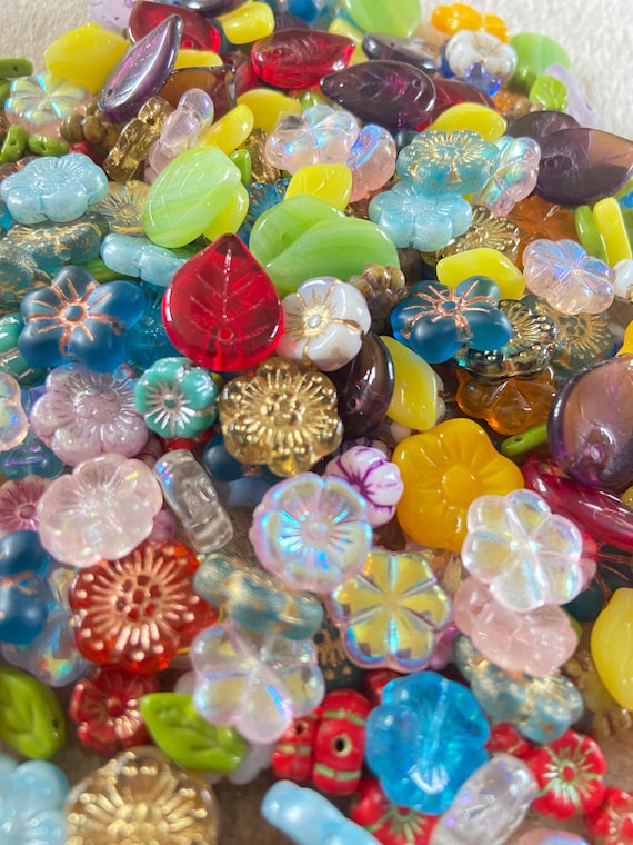A colourful pile of Czech glass flower and leaf beads in shades of pink, red, yellow, green, blue and clear, many.