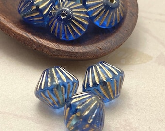 Eight Czech glass tribal bicone beads in blue with gold wash displayed in a wooden bowl and on white background.