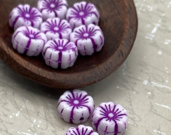 Ten white Czech glass hibiscus flower beads with purple wash detail in a wooden bowl, with three beads displayed separately.