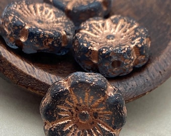 Four grey Czech glass hibiscus flower beads with copper wash sit on a wooden surface, showing their flared petal detail.