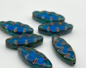 Six Czech glass spindle beads in sea blue with picasso finish, arranged on a plain background