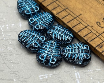 Six black Czech glass trilobite fossil beads with electric blue wash displayed next to a wooden ruler showing size