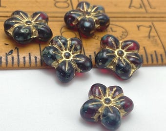 Five deep burgundy Czech glass puffed flower beads with gold wash detailing, displayed on a rustic brown wooden dish against.