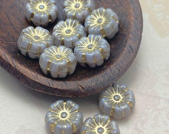 Czech glass hibiscus flower beads in pale lilac with gold wash, about ten beads shown on and beside a wooden dish.