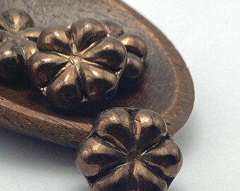 Deep bronze Czech glass flower beads on a wooden dish, showing their rounded petal form and metallic finish.