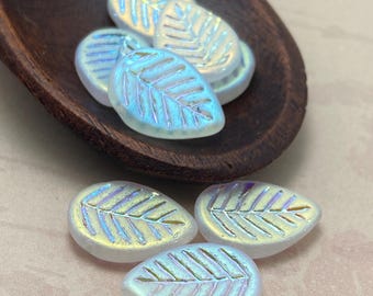 Czech glass leaf beads in white with iridescent shimmer finish, displayed in a dark wooden bowl and on a plain surface.
