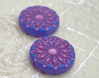 Two purple Czech glass flower coin beads with red-outlined petals lie on a neutral fabric background with a ruler edge.
