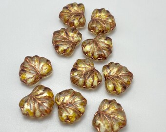 Ten golden topaz Czech glass maple leaf beads with copper details, scattered on a plain grey background.