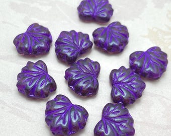 Ten purple Czech glass maple leaf beads with metallic finish arranged on a plain white background.