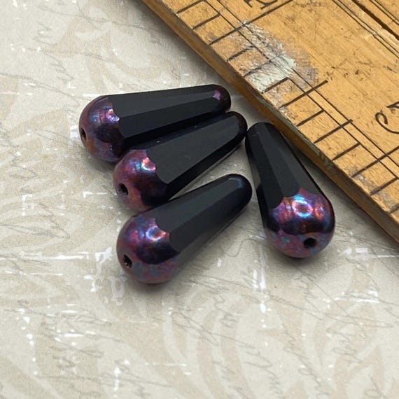 Four Czech glass faceted drop beads in black with purple iridescent accents, shown with a ruler for scale.