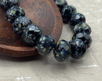 Black Picasso Czech glass rondelle beads arranged on a wooden dish, showing their dark glassy finish with pale speckled.