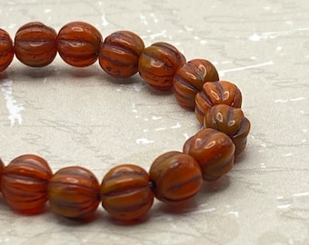 Strand of approximately 25 orange-brown Czech glass melon beads, each with ribbed surface detail, arranged in a loose curve.