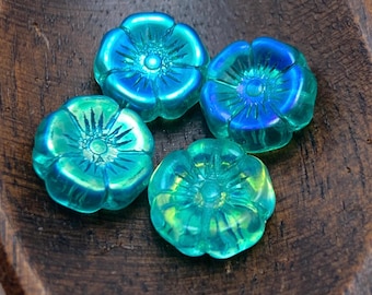 Four translucent Czech glass hibiscus flower beads in teal green with iridescent finish on a dark wooden surface.