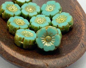 Ten turquoise green hibiscus flower beads with golden stamens arranged on a dark wooden dish.