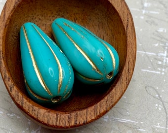 Two turquoise Czech glass melon drop beads with gold lines resting in a wooden bowl.