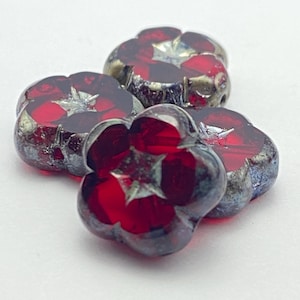 May include: Four flower-shaped beads with a deep red hue and a metallic silver finish. Each bead has five petals and a star-shaped design in the center. The beads are clustered together on a white surface.