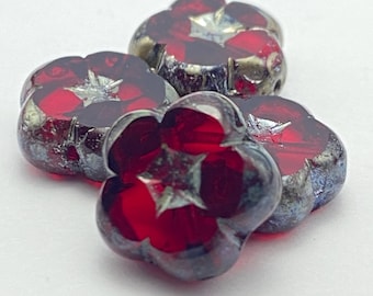 Four ruby red Czech table cut flower beads with picasso finish and silver leaf accents on white background.