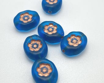 Matte azure blue Czech oval flower beads with copper wash, arranged in a curve next to a ruler for scale.