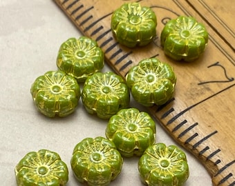 Nine lime green Czech glass Hawaii flower beads with gold wash, arranged on a wooden ruler for scale.