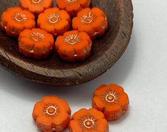Seven bright orange Czech glass flower beads sit in a dark wooden bowl, with three more displayed separately on a white.