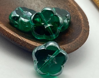 Four emerald green Czech flower beads with silver picasso wash in a wooden bowl next to a ruler for scale.
