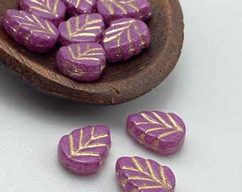 Purple orchid Czech mint leaf beads with gold wash arranged in and below a wooden bowl on a white background.