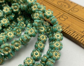 Twelve Czech glass hibiscus flower beads in turquoise with gold wash detail, displayed in a wooden bowl and on a white.
