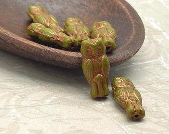 Six olive green Czech glass owl beads with copper wash detail, displayed on a wooden dish.