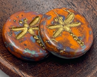 Two Czech dragonfly coin beads, 17mm, rustic orange with blue and gold dragonfly details on a plain background.