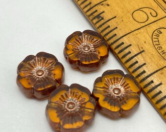 Four amber Czech glass hibiscus flower beads with bronze finish shown against a wooden ruler for scale.