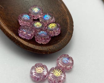 Czech glass hibiscus flower beads in pink crystal with iridescent centres, shown in a wooden spoon and scattered on white.
