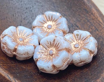 Four white Czech glass hibiscus flower beads with copper wash detailing on a wooden dish.