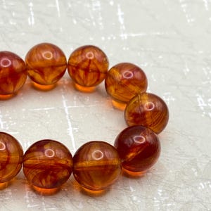 May include: A bracelet made of amber beads with a swirling, marbled pattern in shades of orange and brown.