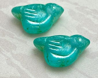 Two Czech glass bird beads in apple green with metallic green wash, shown on a plain fabric background.