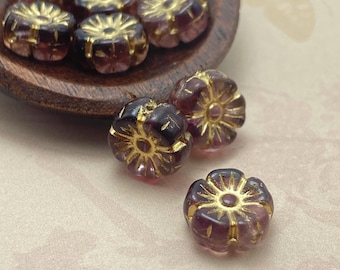 Eight Czech glass hibiscus flower beads in dark plum with gold wash, shown on a wooden dish and cream background.