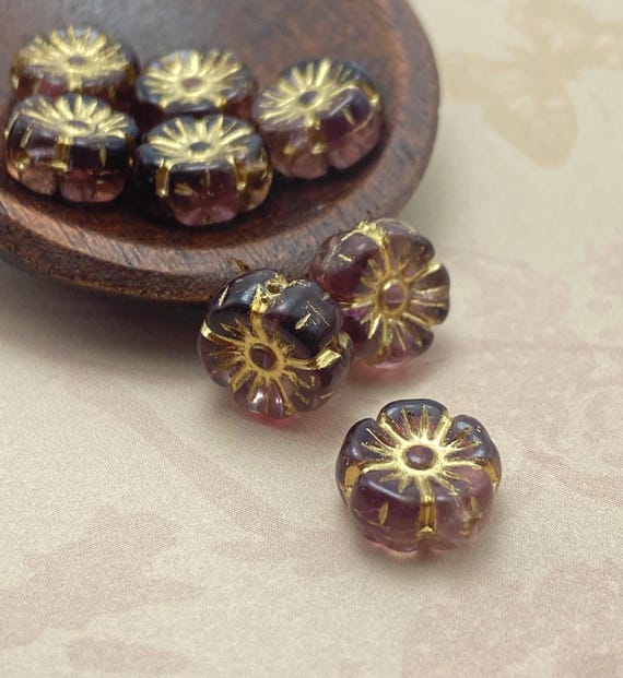 Eight Czech glass hibiscus flower beads in dark plum with gold wash, shown on a wooden dish and cream background.