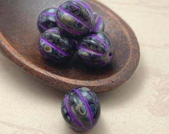 Five Czech glass fluted melon beads in black with purple wash resting in and beside a wooden bowl.